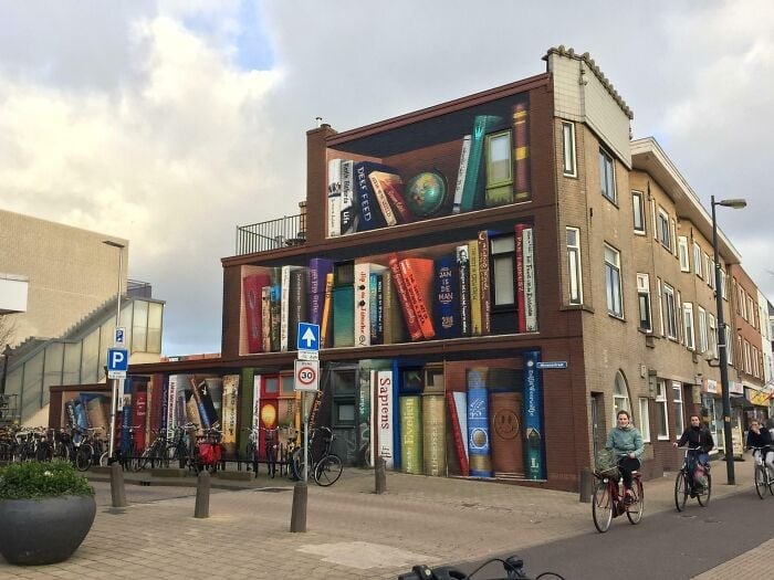 Façade de bâtiment peinte de livres géants et colorés, créant une atmosphère de bibliothèque et de librairie magique dans un cadre urbain.