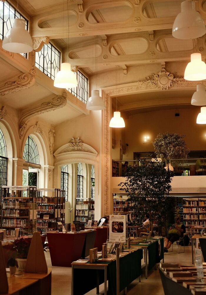 Interior grandioso de biblioteca com tetos altos, arquitetura ornamentada, grandes janelas, estantes de livros e áreas de leitura aconchegantes.