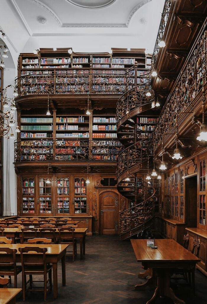 Intérieur grandiose d'une bibliothèque avec étagères en bois, escalier en colimaçon et tables de lecture confortables remplies de livres du monde entier.