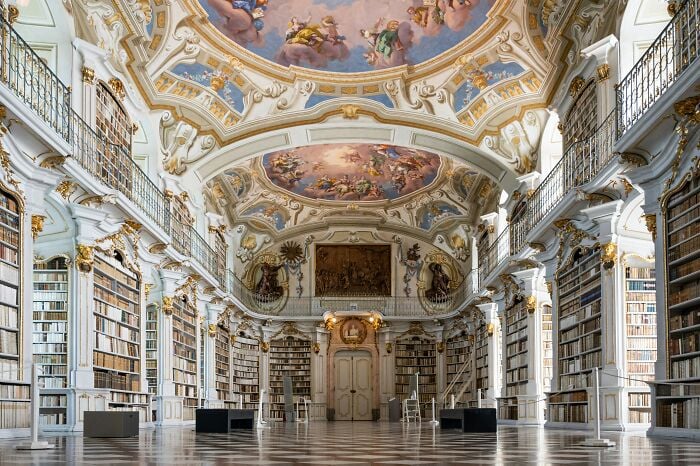 Intérieur grandiose de bibliothèque avec des plafonds ornés et de hautes étagères remplies de livres dans une atmosphère magique.