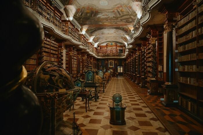 Intérieur grandiose de la bibliothèque avec des globes antiques, des colonnes ornées et des rangées de vieux livres sur des étagères en bois.
