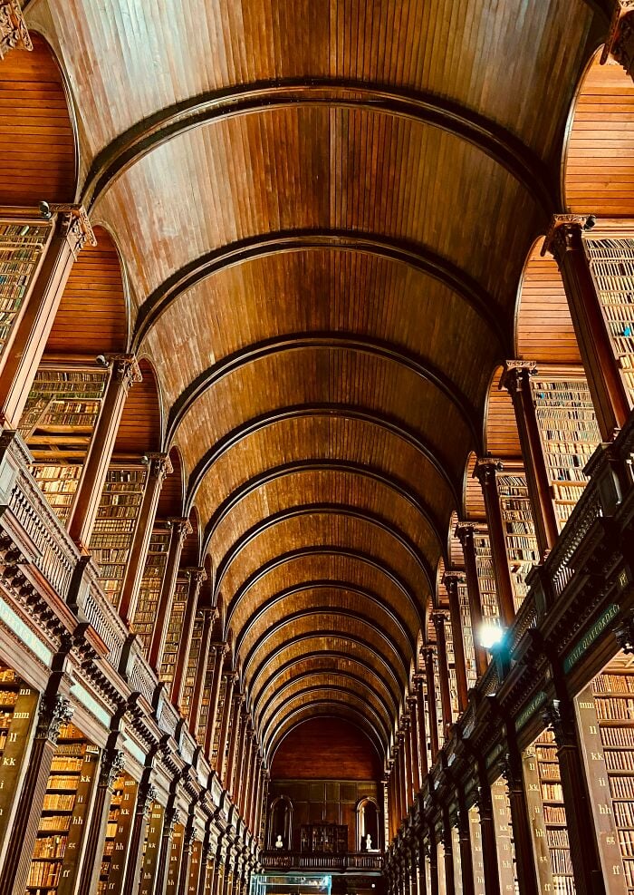 Intérieur de bibliothèque grandiose avec un haut plafond voûté en bois et de hautes étagères remplies de livres du sol au plafond.